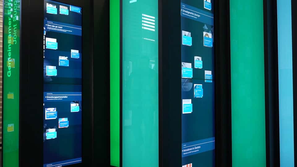 Close-up view of multiple vertical touchscreens within the BASF History Library installation, showing dense, data-driven historical content arranged across tall, book-like display columns.
