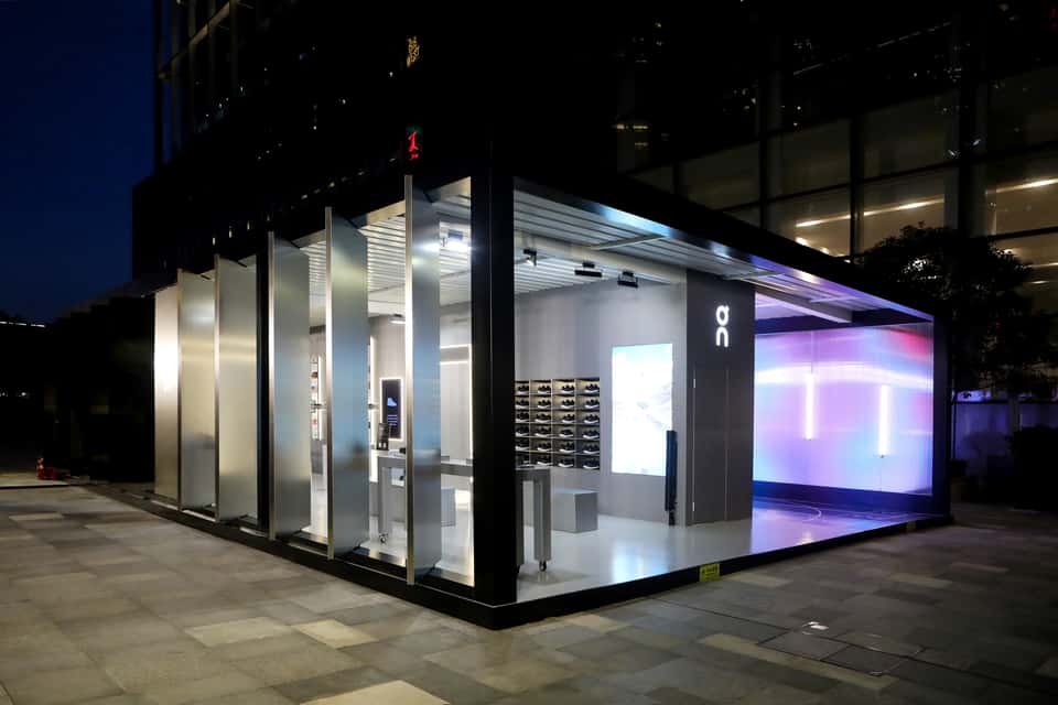 An On Running store at night, showing the LED wall through the storefront windows.